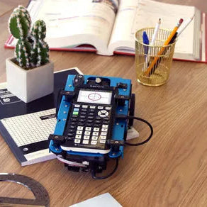 Texas Instruments calculator on a desk with a notebook, protractor, cactus, and school supplies