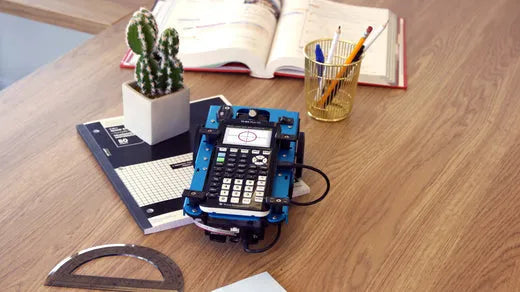 Texas Instruments calculator on a desk with a notebook, protractor, cactus, and school supplies