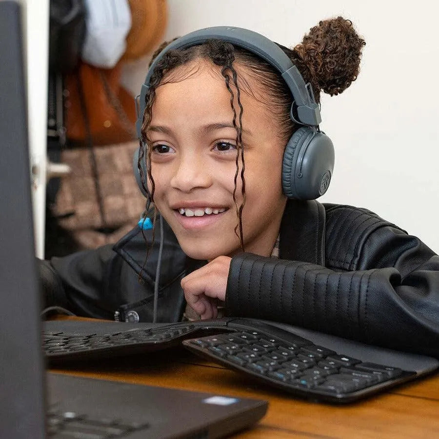 Smiling child wearing JLab JBuddies kids headphones using a computer at a desk