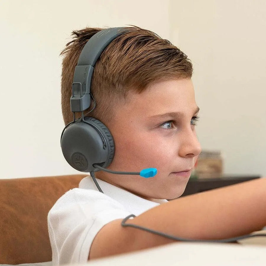 Young boy using JLab JBuddies kids headphones with microphone at desk, Underwood Distributing