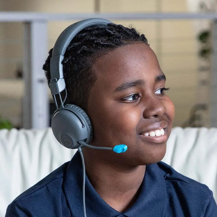 Smiling child wearing JLab JBuddies Learn on-ear kids headphones with microphone indoors