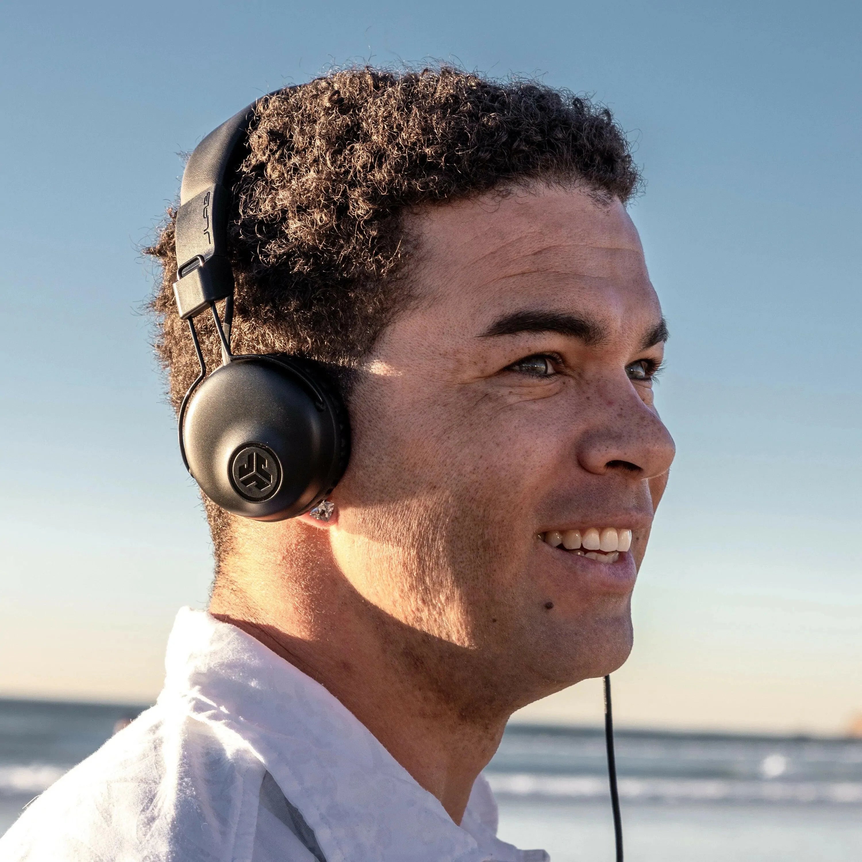 Man smiling outdoors wearing black JLab Studio headset by the ocean, Underwood Distributing Co.