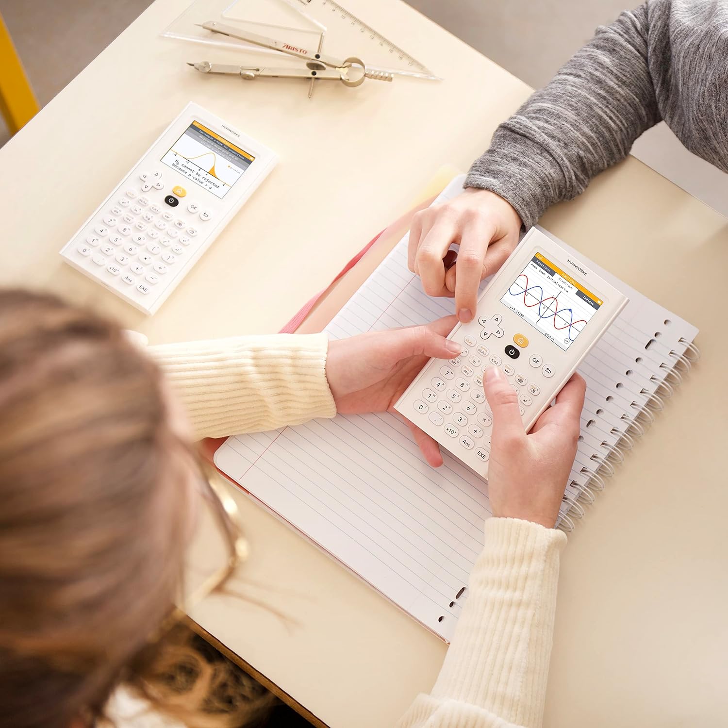 Students using NumWorks graphing calculators over notebooks at a desk, Underwood Distributing Co.