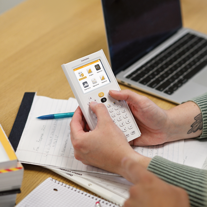 Person using NumWorks graphing calculator at desk with notes, pen, and laptop, Underwood Distributing Co.