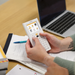 Person using NumWorks graphing calculator at desk with notes, pen, and laptop, Underwood Distributing Co.